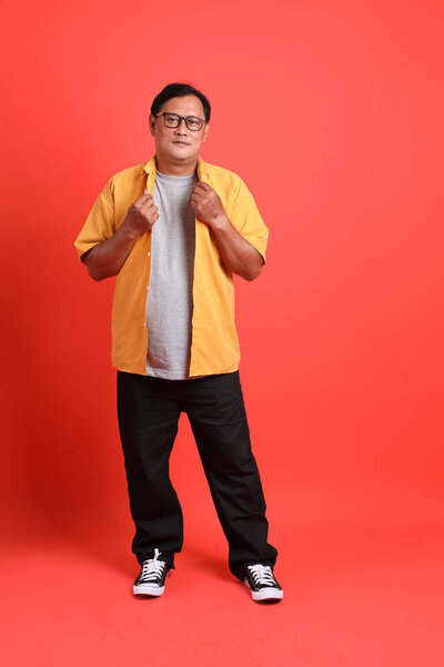 The adult Asian man with yellow shirt standing on the orange background.