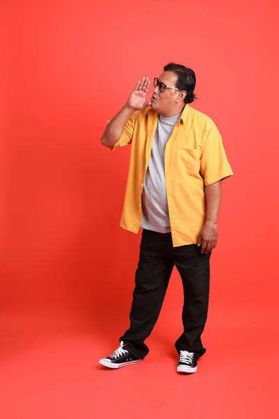 The adult Asian man with yellow shirt standing on the orange background.