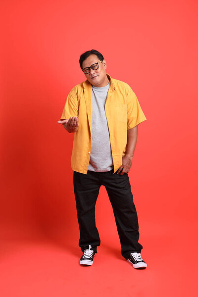 The adult Asian man with yellow shirt standing on the orange background.