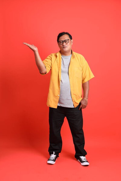The adult Asian man with yellow shirt standing on the orange background.