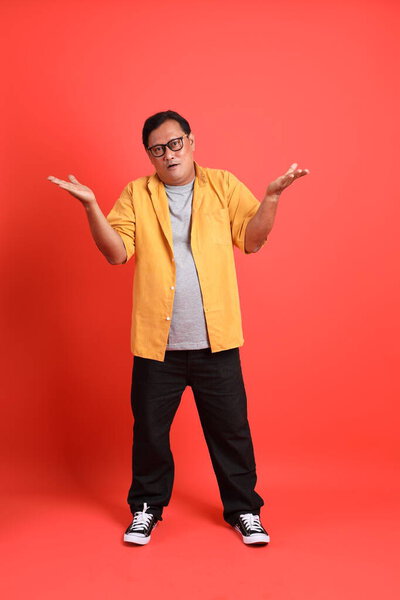 The adult Asian man with yellow shirt standing on the orange background.