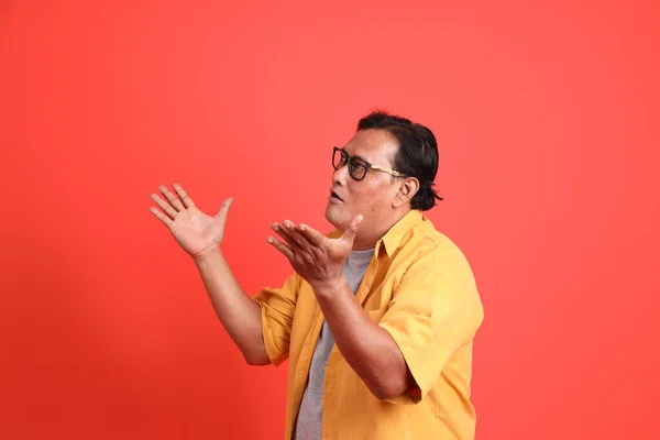 The adult Asian man with yellow shirt standing on the orange background.