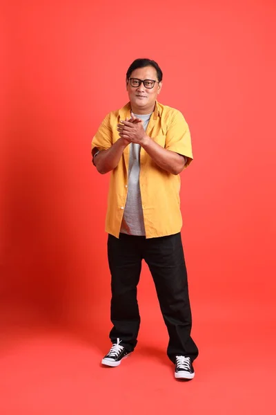 The adult Asian man with yellow shirt standing on the orange background.