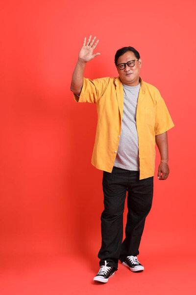 The adult Asian man with yellow shirt standing on the orange background.