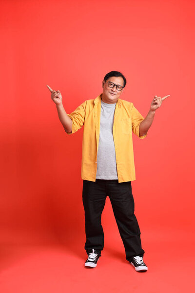 The adult Asian man with yellow shirt standing on the orange background.