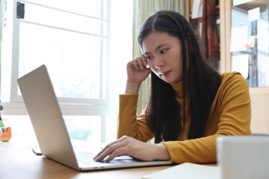 The Asian adult woman working on laptop in her home studio.