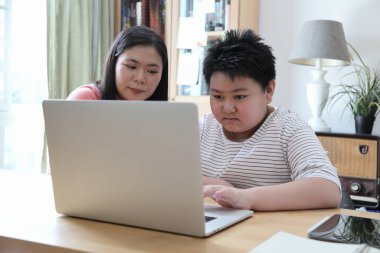 Asyalı bekar anne, oğlunun evde öğrenmesine yardım ediyor..