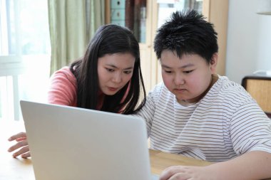 Asyalı bekar anne, oğlunun evde öğrenmesine yardım ediyor..