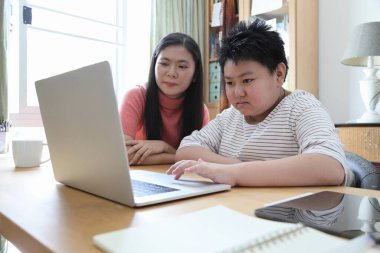 Asyalı bekar anne, oğlunun evde öğrenmesine yardım ediyor..