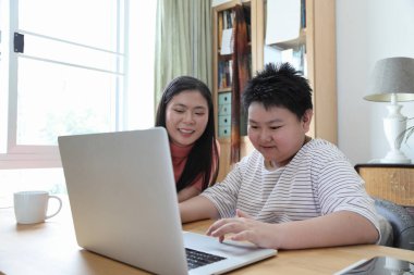 Asyalı bekar anne, oğlunun evde öğrenmesine yardım ediyor..