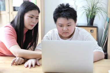 Asyalı bekar anne, oğlunun evde öğrenmesine yardım ediyor..