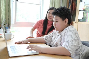 Asyalı bekar anne, oğlunun evde öğrenmesine yardım ediyor..