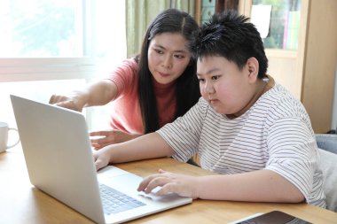 Asyalı bekar anne, oğlunun evde öğrenmesine yardım ediyor..