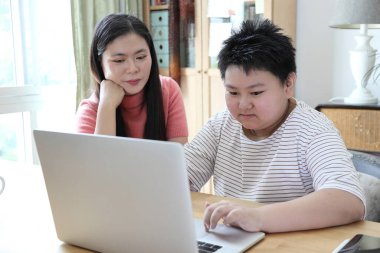 Asyalı bekar anne, oğlunun evde öğrenmesine yardım ediyor..