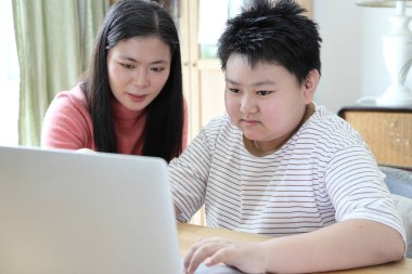 Asyalı bekar anne, oğlunun evde öğrenmesine yardım ediyor..