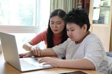 Asyalı bekar anne, oğlunun evde öğrenmesine yardım ediyor..