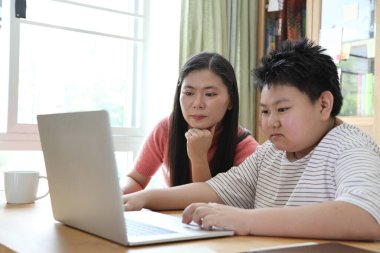 Asyalı bekar anne, oğlunun evde öğrenmesine yardım ediyor..