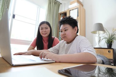 Asyalı bekar anne, oğlunun evde öğrenmesine yardım ediyor..