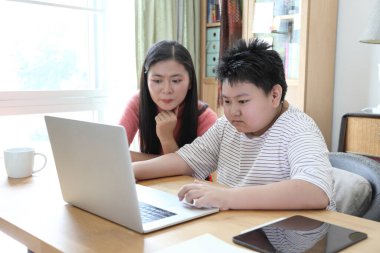 Asyalı bekar anne, oğlunun evde öğrenmesine yardım ediyor..