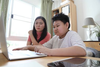 Asyalı bekar anne, oğlunun evde öğrenmesine yardım ediyor..