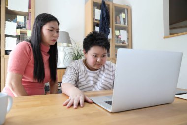 Asyalı bekar anne, oğlunun evde öğrenmesine yardım ediyor..