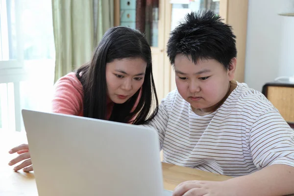 Asyalı bekar anne, oğlunun evde öğrenmesine yardım ediyor..