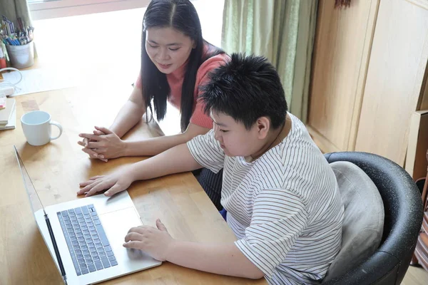 Asyalı bekar anne, oğlunun evde öğrenmesine yardım ediyor..