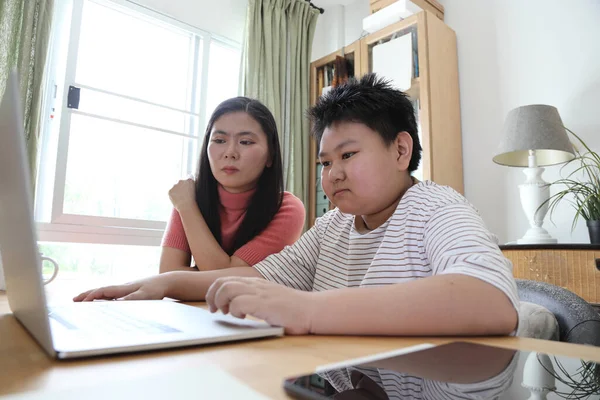 Asyalı bekar anne, oğlunun evde öğrenmesine yardım ediyor..