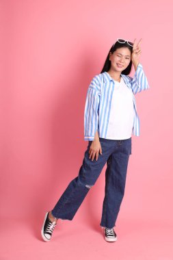 The Asian adult woman with casual clothes standing on the pink background.