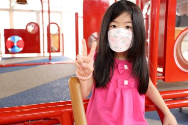 The little Asian girl playing in the playground with mask on the face.