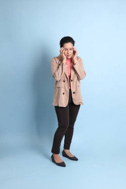 Mavi arka planda pembe gömlekli, kahverengi ceketli son sınıf Asyalı kadın..