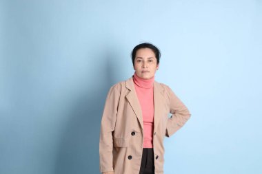 Mavi arka planda pembe gömlekli, kahverengi ceketli son sınıf Asyalı kadın..