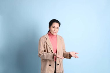 Mavi arka planda pembe gömlekli, kahverengi ceketli son sınıf Asyalı kadın..