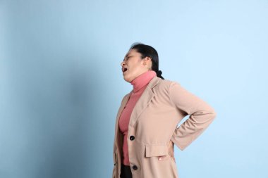 Mavi arka planda pembe gömlekli, kahverengi ceketli son sınıf Asyalı kadın..