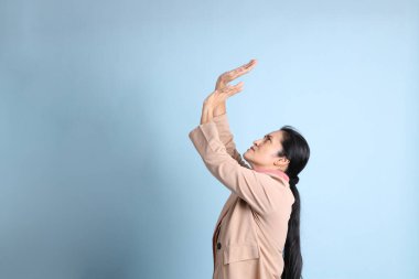 Mavi arka planda pembe gömlekli, kahverengi ceketli son sınıf Asyalı kadın..