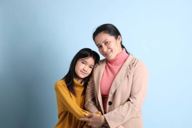 Yaşlı Asyalı kız mavi arka planda annesine sarılıyor..