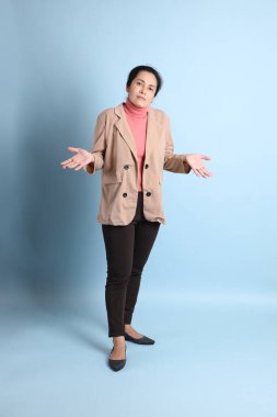 Mavi arka planda pembe gömlekli, kahverengi ceketli son sınıf Asyalı kadın..