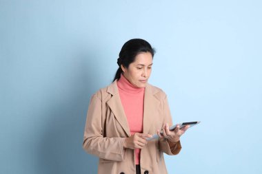 Mavi arka planda pembe gömlekli, kahverengi ceketli son sınıf Asyalı kadın..