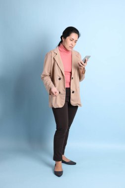 Mavi arka planda pembe gömlekli, kahverengi ceketli son sınıf Asyalı kadın..