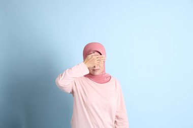 Mavi arka planda tesettürlü Güneydoğu Asyalı yaşlı kadın.