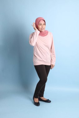 Mavi arka planda tesettürlü Güneydoğu Asyalı yaşlı kadın.