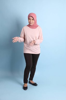 Mavi arka planda tesettürlü Güneydoğu Asyalı yaşlı kadın.