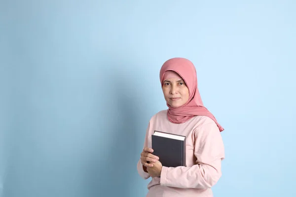 The senior southeast Asian woman with hijab standing on the blue background