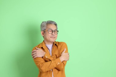 40 'lı yaşlarda yeşil arka planda duran sarı gömlekli Asyalı bir adam..