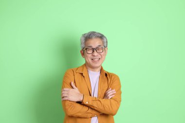 40 'lı yaşlarda yeşil arka planda duran sarı gömlekli Asyalı bir adam..