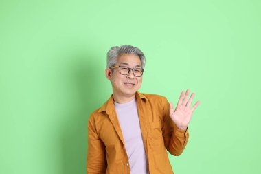 40 'lı yaşlarda yeşil arka planda duran sarı gömlekli Asyalı bir adam..