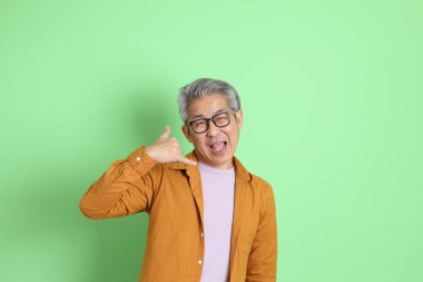 40 'lı yaşlarda yeşil arka planda duran sarı gömlekli Asyalı bir adam..