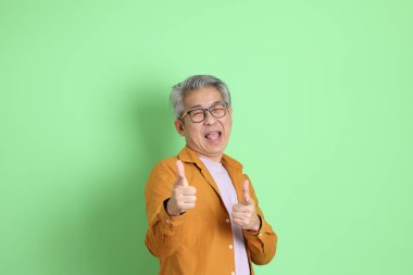 40 'lı yaşlarda yeşil arka planda duran sarı gömlekli Asyalı bir adam..