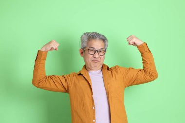 40 'lı yaşlarda yeşil arka planda duran sarı gömlekli Asyalı bir adam..