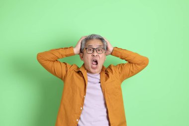 40 'lı yaşlarda yeşil arka planda duran sarı gömlekli Asyalı bir adam..